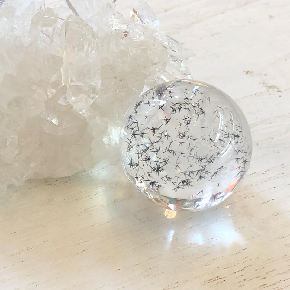 白木の机に置いた、針状の結晶が入った水晶の丸玉